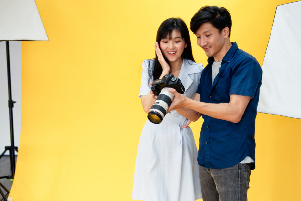 在幕后，摄影师正在检查照片，美丽的年轻女模特微笑着在工作室的背景和灯光摆姿势。有选择性的重点图片下载