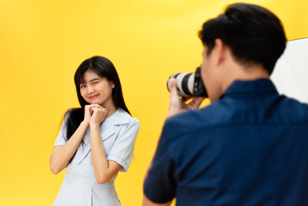 在幕后，摄影师们用相机和镜头拍摄美丽的年轻女模特在工作室的背景和灯光下微笑和摆姿势的照片。有选择性的重点图片下载