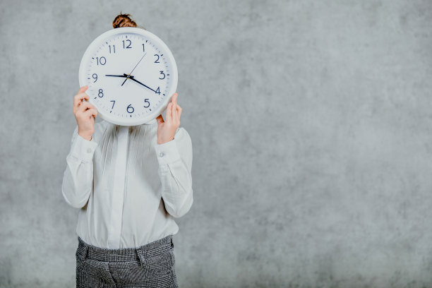 灰色背景上的一个小女孩的照片。现代商业女孩拿着手表挡在面前。图片下载