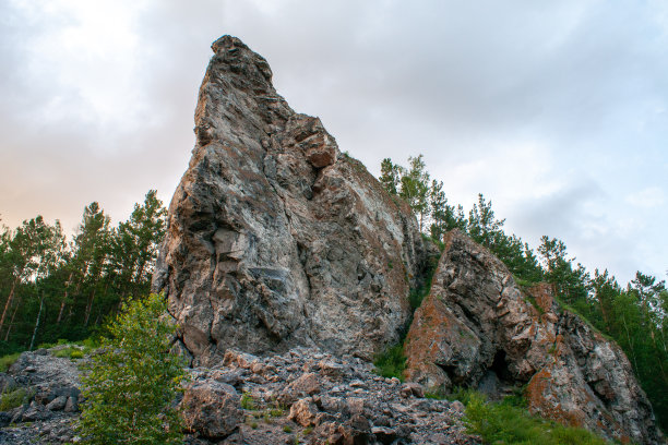 陡峭的岩石在多云的天空和树木的背景。特写镜头图片下载