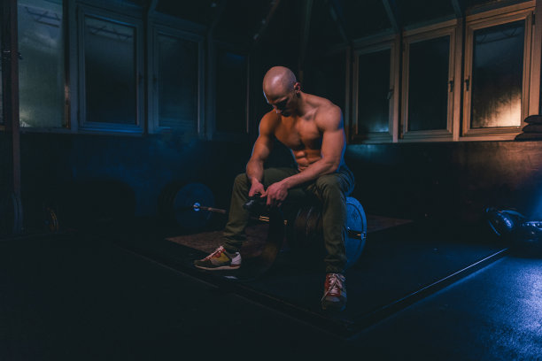 赤裸上身的男人坐在黑暗的健身房举重图片下载