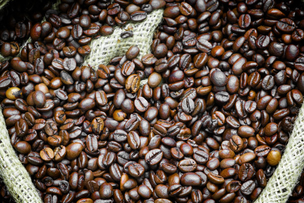 烤咖啡豆落在粗麻袋里。麻袋与咖啡豆，背景。咖啡出口。图片下载