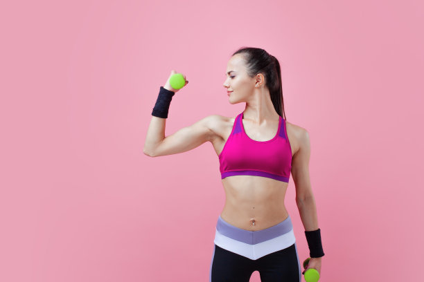 一个年轻的运动迷人的黑发女孩扎着马尾辫，手里拿着哑铃，展示着她的二头肌。女孩的力量。图片下载