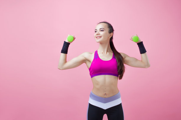 一个年轻的运动迷人的黑发女孩扎着马尾辫，手里拿着哑铃，展示着她的二头肌。女孩的力量。图片下载
