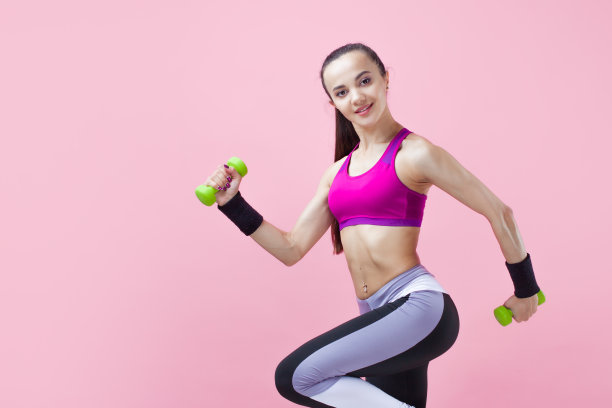 年轻的运动型黑发女孩穿着鲜艳的运动上衣，扎着马尾辫，拿着绿色的哑铃，飘动着头发。图片下载