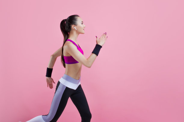 一个年轻迷人的女孩微笑着跑着，戴着无线耳机，穿着明亮的运动上衣，粉红色的背景，有氧运动。图片下载