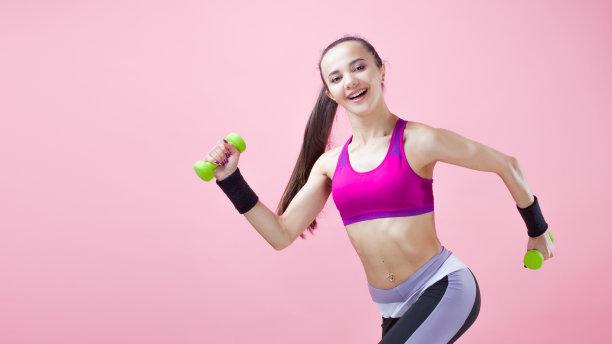 年轻的运动型黑发女孩穿着鲜艳的运动上衣，扎着马尾辫，拿着绿色的哑铃，飘动着头发。图片下载