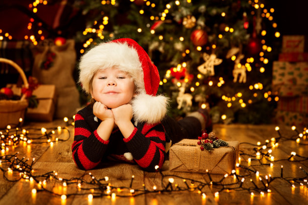 圣诞小孩儿在红帽，快乐的孩子肖像在装饰照明室，圣诞宝贝男孩和礼物图片下载