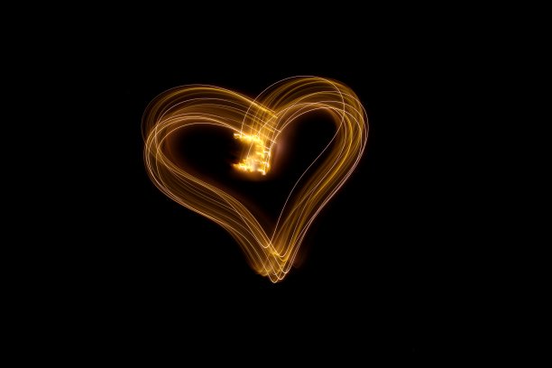 长曝光照片的心轮廓在霓虹灯金色抽象漩涡心形状轮廓，平行线模式在黑色的背景。光绘摄影。图片下载