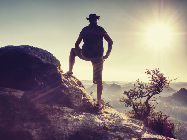 穿着户外衣服和靴子的运动员在岩石山峰上行走。图片下载