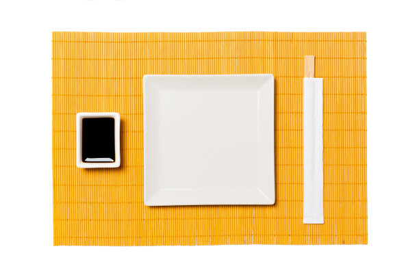 用筷子夹寿司和酱油的白色方形盘子放在黄色的竹席上。顶视图与复制空间为您设计图片下载