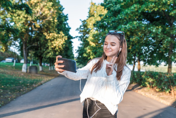 少女12-15岁，夏天城市公园秋天，照片自己在电话，视频通话，快乐的微笑欣喜，应用在线互联网牛仔裤毛衣太阳镜，听音乐耳机。图片下载