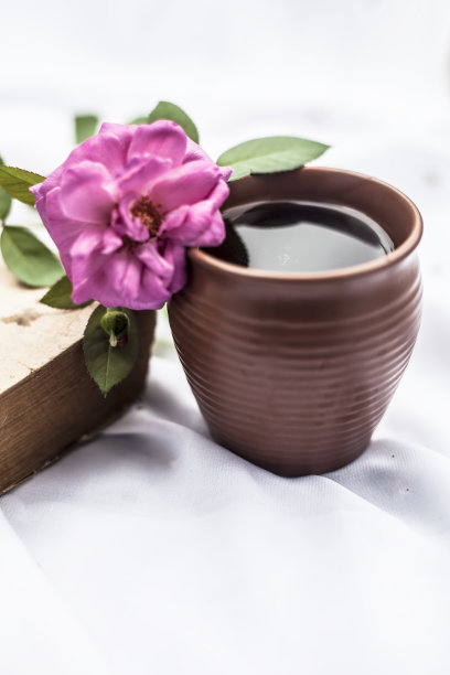 古董旧书白色织物与单一的粉红色玫瑰和一些咖啡在一个黏土杯孤立。图片下载