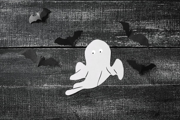 黑色的木头背景上的白色鬼魂服装。简约的万圣节的概念。牛皮纸鬼魂图片下载