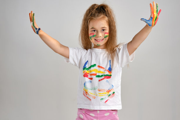 小女孩穿着白色彩绘t恤，孤立地站在白色上，用她不同颜色的彩绘手势手掌和脸。艺术工作室。特写镜头图片下载