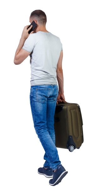 带着行李箱走路的人用智能手机说话的背影。图片下载