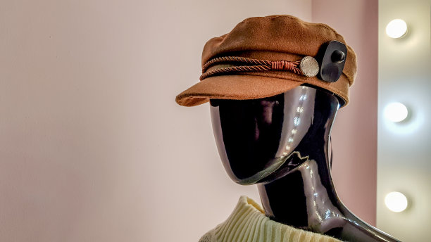 一个戴着棕色帽子的黑色人体模特在一家女装店的肖像。粉色墙壁背景上的戴着帽子的女模特和一面带有背光和灯泡的白色大镜子图片下载