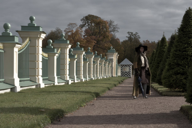 法国黑色风格的照片，一个年轻美丽的女人摆姿势在长长的绿色和棕色礼服大衣在花园的宫殿在Oranienbaum附近的圣彼得堡，俄罗斯图片下载
