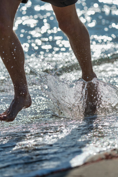 在一个阳光明媚的日子里，一个男孩沿着海边奔跑时溅起水花的腿的照片细节。健康生活的概念。图片下载