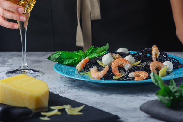 墨鱼墨黑色意大利面。马苏里拉虾仁意大利面和罗勒。一个女孩喝着酒的照片。图片下载