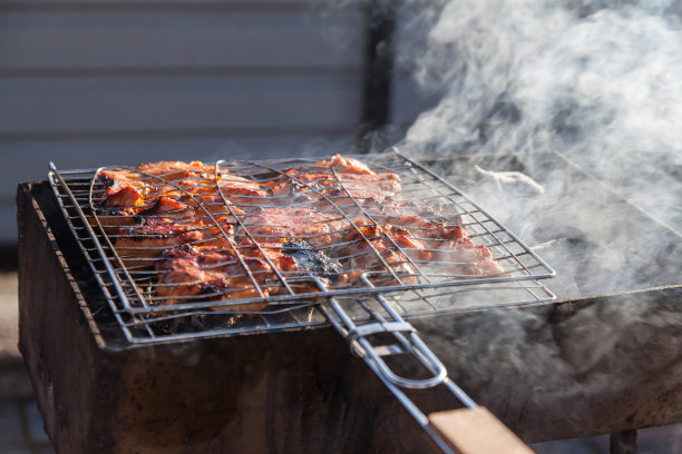 特写猪肉或牛肉串的烹饪过程，夹在烤架上，烤架上有一层酥脆的焦皮，盖在灰色的炭火上，烟雾不断上升。图片下载