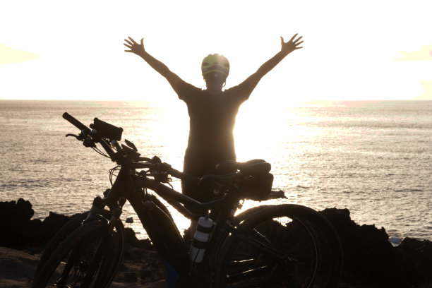 后视图的资深活跃妇女在大海在日落。黑色的轮廓。武器了。自由和幸福的概念。黄色头盔。健康的生活方式图片下载