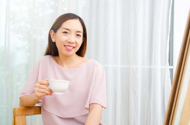 微笑的女人女艺术家在画布上画的油画在我的家作为她的爱好，看图片喝咖啡。图片下载