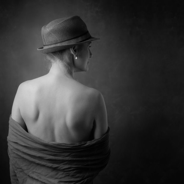 一个美丽的成熟女人的肖像赤裸的肩膀。戴着帽子的迷人的苗条女人转过身去。图片下载