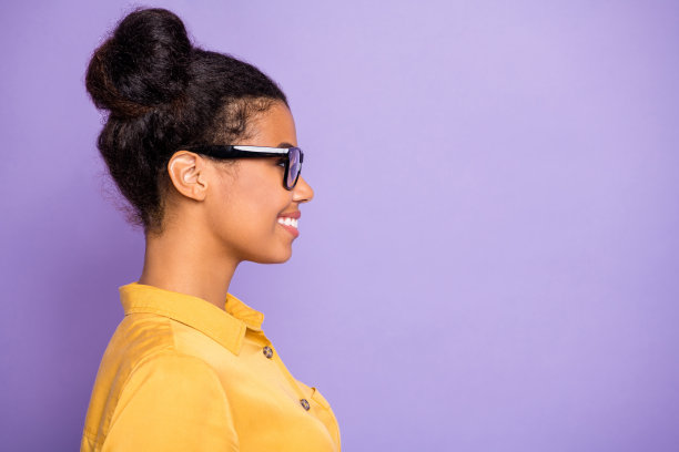 个人资料照片漂亮的黑皮肤商务女士聪明的眼睛看着空的空间笑容，露齿的微笑戴眼镜黄衬衫孤立的紫色背景图片下载