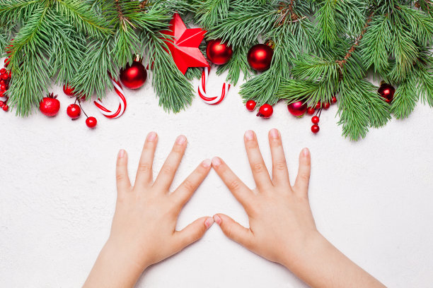 圣诞卡与绿色的圣诞冷杉枝，红色的冬青浆果，小玩意和婴儿女孩的手在白色的背景图片下载