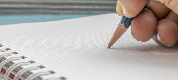 特写一名亚洲男子的手正在用木铅笔在格子线笔记本上写字图片下载