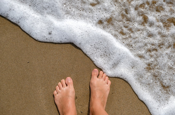 女人的脚站在沙滩上的沙与波浪。图片下载
