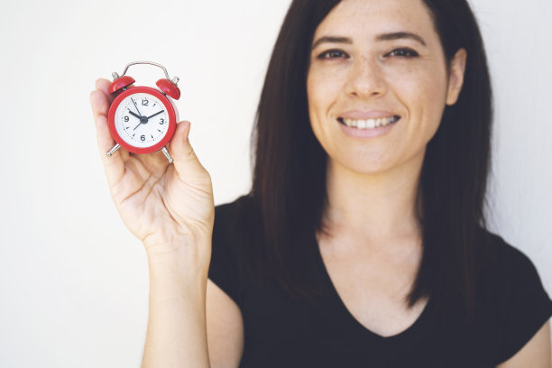 快乐的年轻女子在黑色的t恤，一个拿着红色的闹钟和挥舞的手孤立在白色图片下载