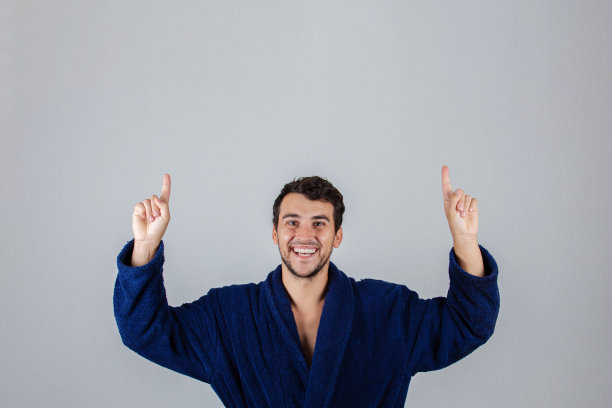 肖像欢快的年轻人，积极的微笑指向向上的姿态，穿着蓝色浴衣，孤立在白色的背景。图片下载