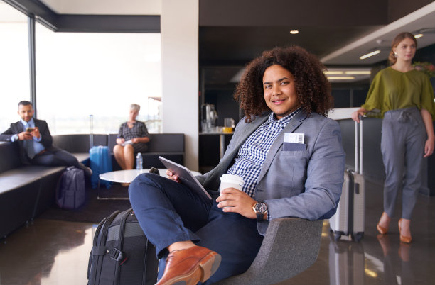 一个非裔美国人坐在现代机场的候机室里，带着行李坐在平板电脑上图片下载