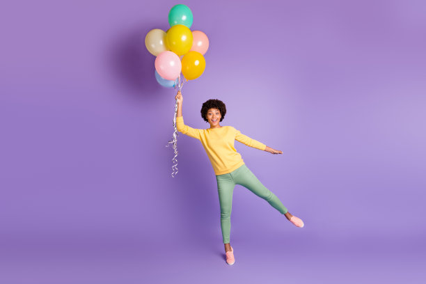 这是一张激动、有趣、时髦的美国黑人女孩的全长照片，她拿着热气球，以为自己会在天空中飞行，穿着休闲风格的衣服，孤立在紫罗兰色的背景下图片下载