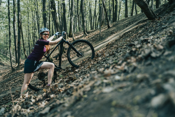女运动员在森林里戴着头盔骑自行车上山的照片图片下载