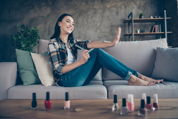 头像照片可爱的女士纠正指甲形状与指甲文件满意的结果将应用红色指甲油穿休闲衣服坐在舒适的沙发公寓室内图片下载