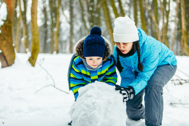 母亲和蹒跚学步的儿子堆雪人。滚动的大雪球。冬季休闲活动图片下载