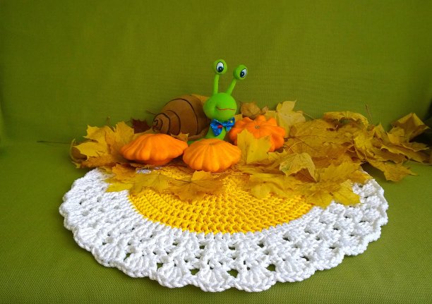 舒适的秋天装饰。手工编织的老式餐巾在黄色和白色。有趣的毛绒玩具蜗牛。由落下的枫叶、橙色南瓜和南瓜组成。绿色背景。舒适的家。图片下载