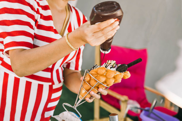 一个穿着红白相间裙子的女孩正在准备美味的甜点。香港华夫饼冰淇淋。在上面倒入糖浆。图片下载