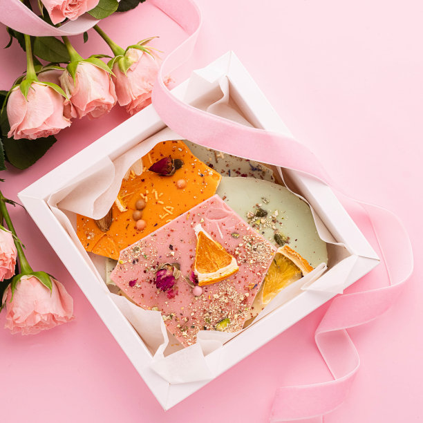 粉色背景上的不同颜色手工巧克力和一束玫瑰。独家甜点的礼物。图片下载