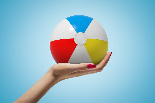 在蓝色的背景下，女性手拿着彩色的沙滩球图片下载