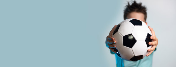一个穿着蓝色t恤的男孩，手里拿着一个足球，掩盖了他的头在蓝色的背景图片下载