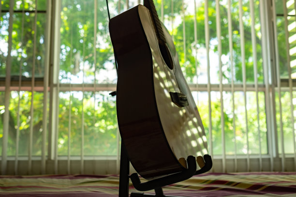 木吉他在床上俯瞰树的窗户。图片下载