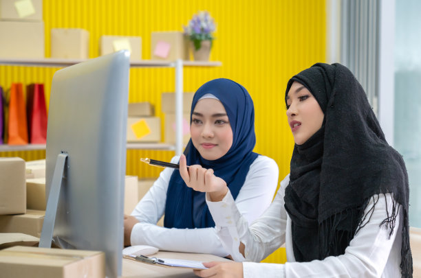 两个年轻的亚洲穆斯林妇女穿着头巾在家里工作，检查产品的订单在电脑和网上营销包装盒和中小企业的概念图片下载