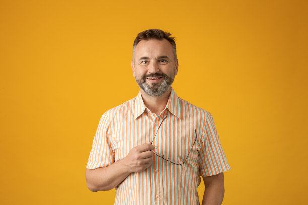 这是一幅50岁大胡子男子的照片，他穿着条纹夏装，黄色背景上戴着眼镜图片下载