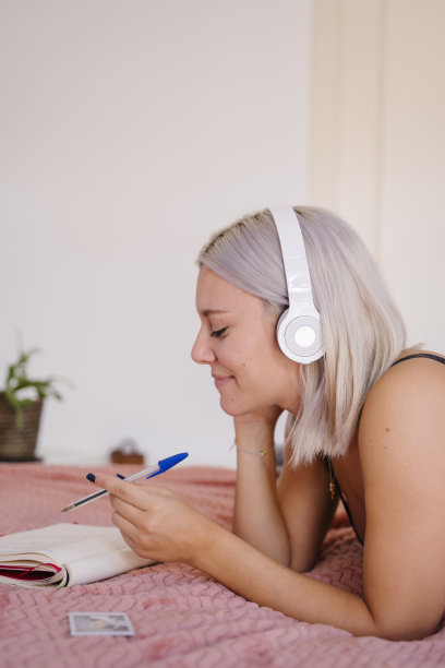 年轻美丽的白人女人躺在床上听着音乐，放松着。图片下载