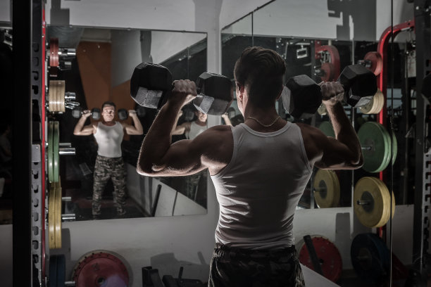 一个强壮的男人在镜子旁边举起哑铃图片下载