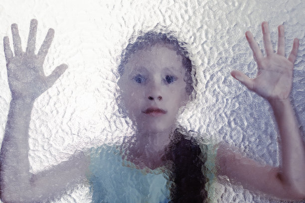 小女孩躲在玻璃后面，双手放在玻璃上图片下载